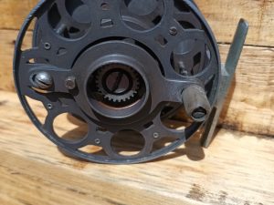 A fly reel sitting on top of a wooden table.